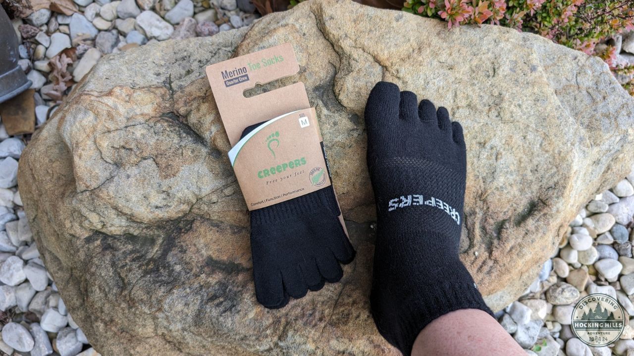 A foot on a rock wearing a Merino wool toe sock from Creepers, next to a package of Creepers socks.