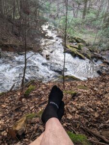 Creepers Merino wool toe socks with feet propped on rock overlooking a flowing creek.